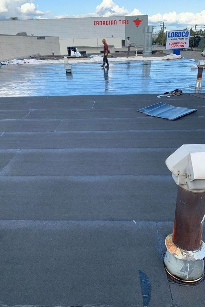 Torch-on membrane installation on a commercial flat roof with vents, flashing and reflective underlayment