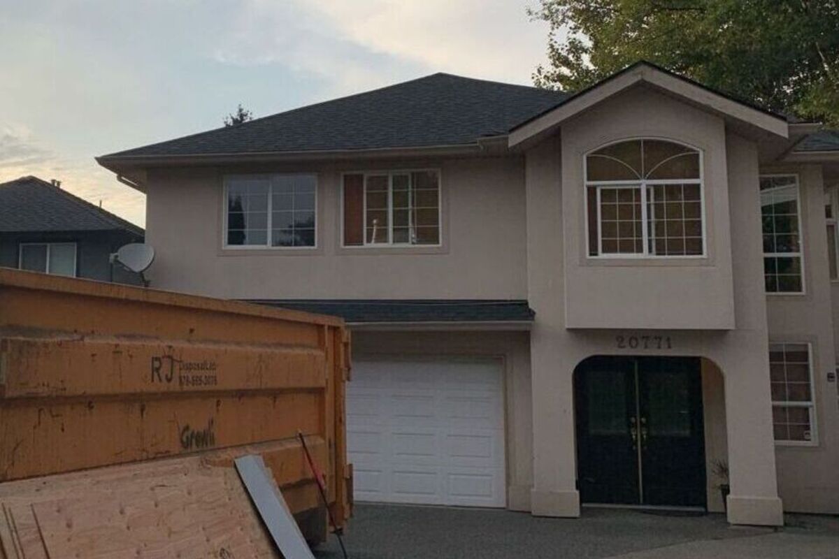 Home with dark asphalt shingles after roof replacement in Vancouver and disposal bin in the driveway