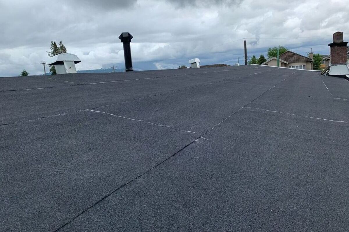 Residential low-slope roof with dark torch-on membrane, vents, chimney flashing and sealed seams