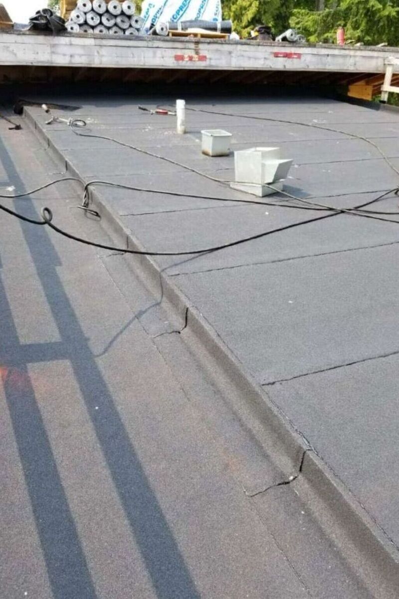 Torch-on roofing installation in Vancouver with gray membrane sheets, roof penetrations and rolled materials nearby