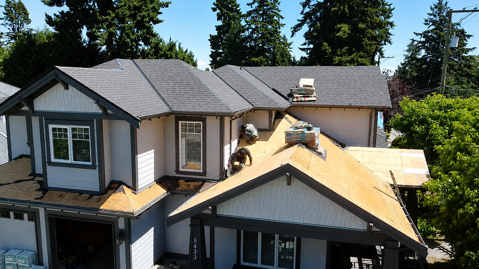 Roofing crew installing asphalt shingles on a North Vancouver home with exposed plywood decking and new roofing materials.