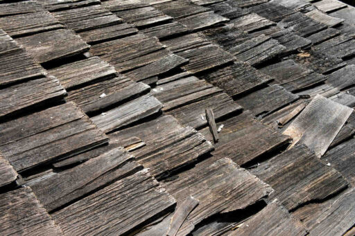 Close-up of an old cedar shake roof with cracked, curled, split, and weathered wood shakes showing visible roof deterioration.