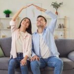 Homeowners sitting on a couch forming a roof shape with their hands, symbolizing home protection and roof warranty coverage