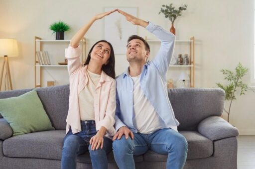 Homeowners sitting on a couch forming a roof shape with their hands, symbolizing home protection and roof warranty coverage