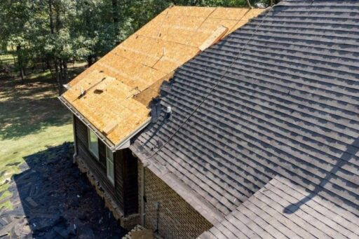 Residential roof partially stripped, showing new plywood roof sheathing beside existing asphalt shingles