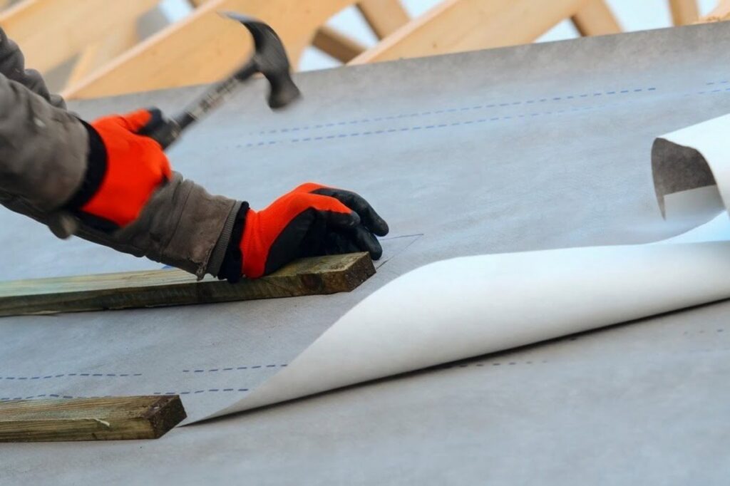 Synthetic roof underlayment being installed over the roof deck before shingles or metal roofing