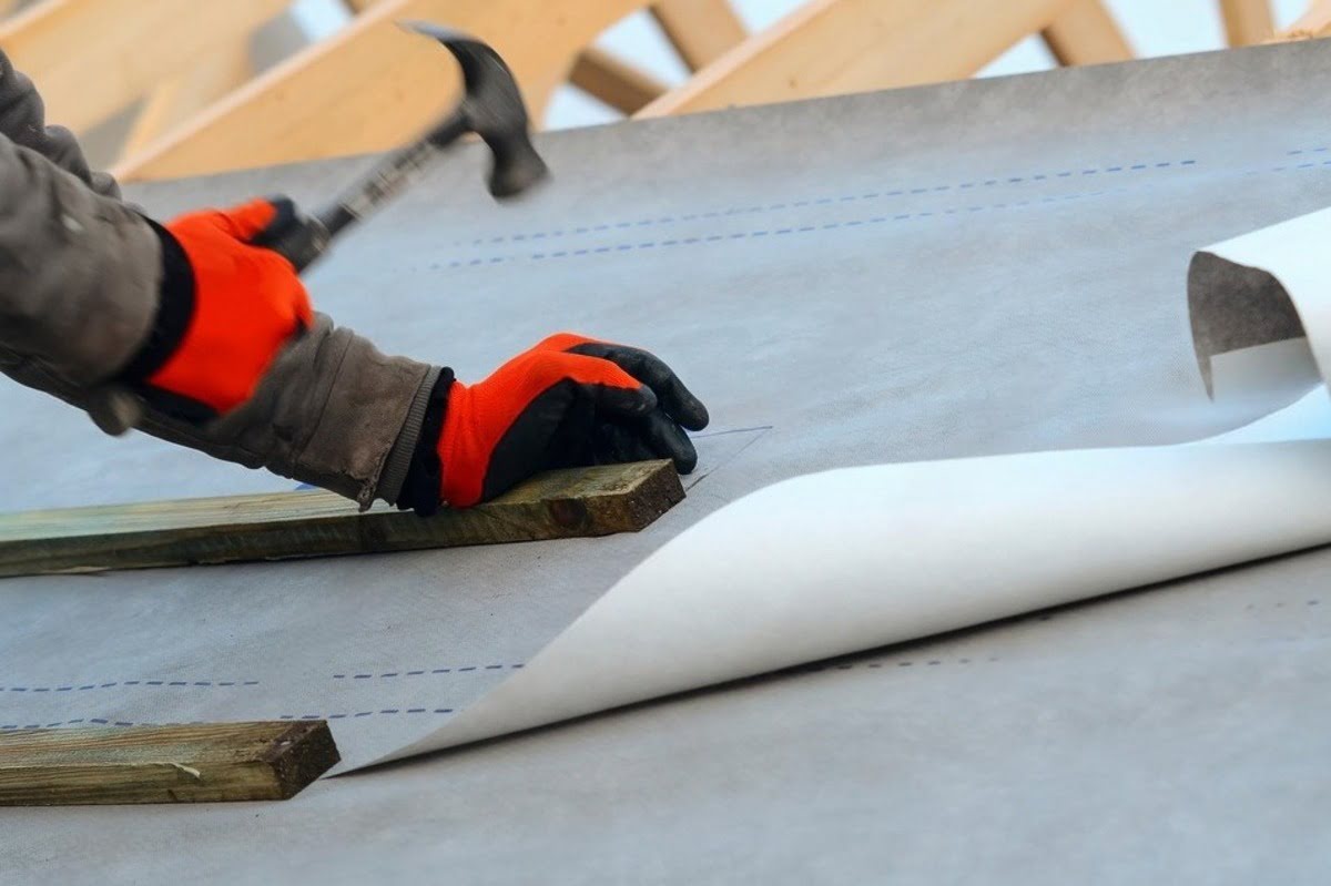 Synthetic roof underlayment being installed over the roof deck before shingles or metal roofing